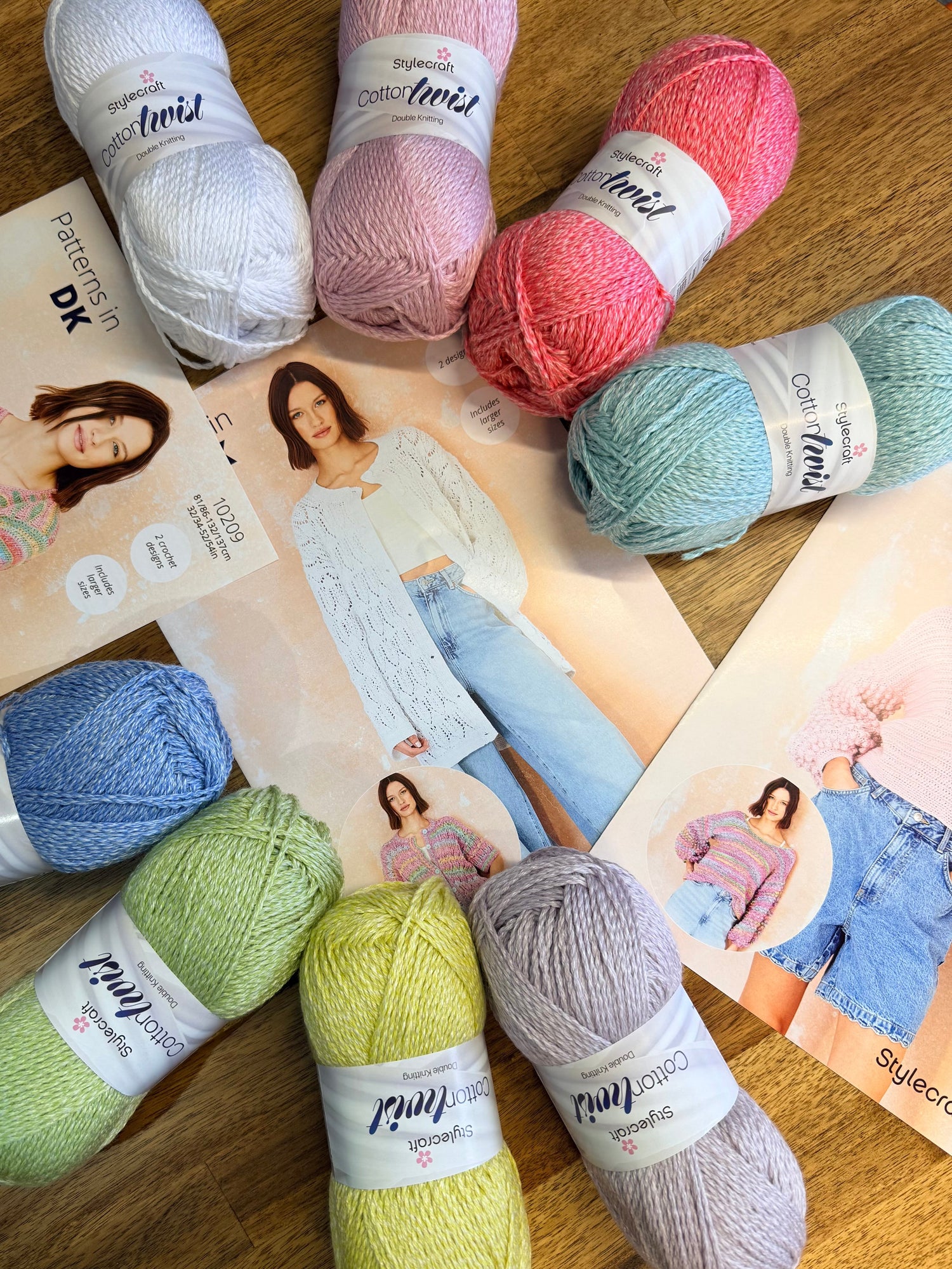 Stylecraft cotton twist yarn in various pastel colours(white, baby pink, pink, mint, blue, green, yellow, grey) arranged around knitting pattern booklets.